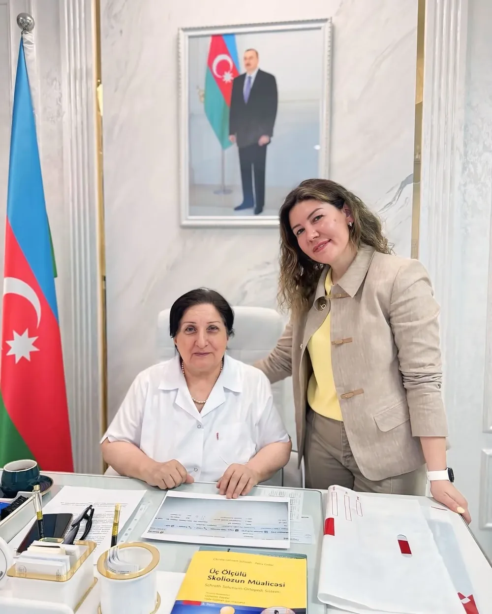 Dr. Elfanə Süleymanova və həmkarı, masada «Üç Ölçülü Skoliozun Müalicəsi — Schroth Salınım-Ortopedi Sistemi» kitabı